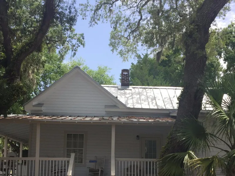 White historic cottage with a tin roof and front porch under live oaks in Apalachicola