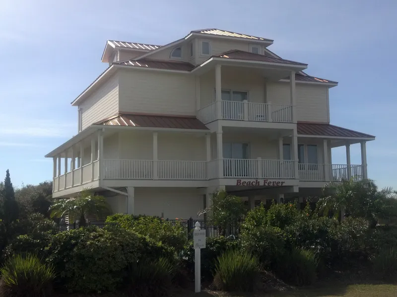 Tall cream coastal home with layered porches rising above dune grasses