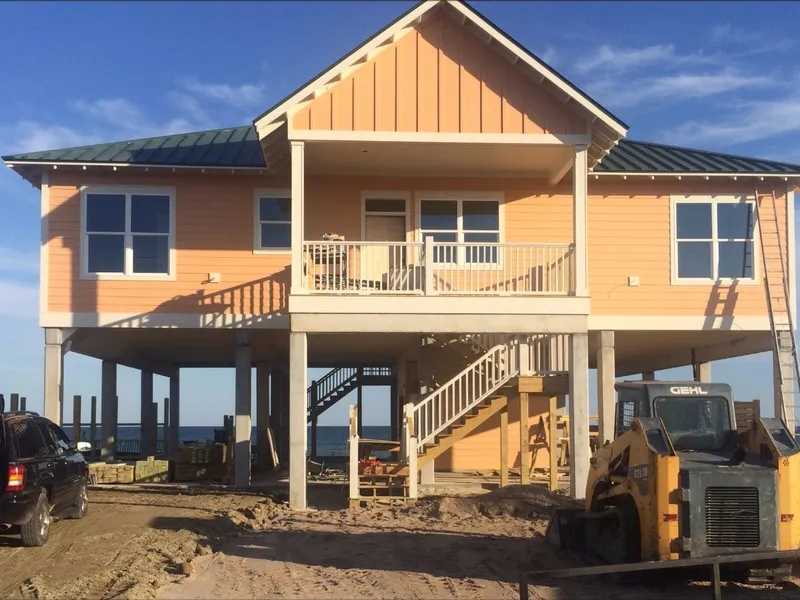 Orange beach house on pilings with a green roof and stair to a wide porch