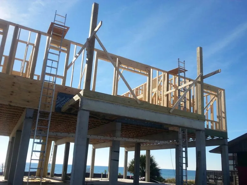 Wood framing of a new house rising on concrete pilings beside the Gulf