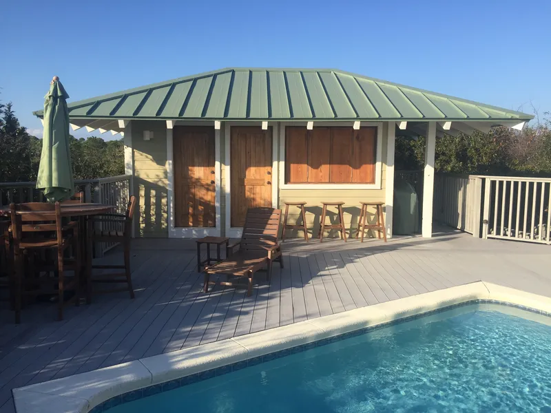 Pool house with a green metal roof, wood doors and a deck beside a swimming pool