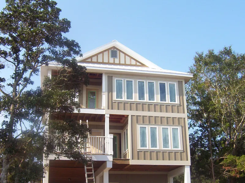 Tall board-and-batten coastal home with bands of windows among trees